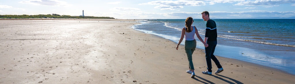 A picture of a couple walking along a beach in Moray Speyside