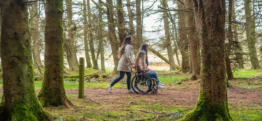 A Lady Pushing Another Lady's Wheelchair Through a Forest