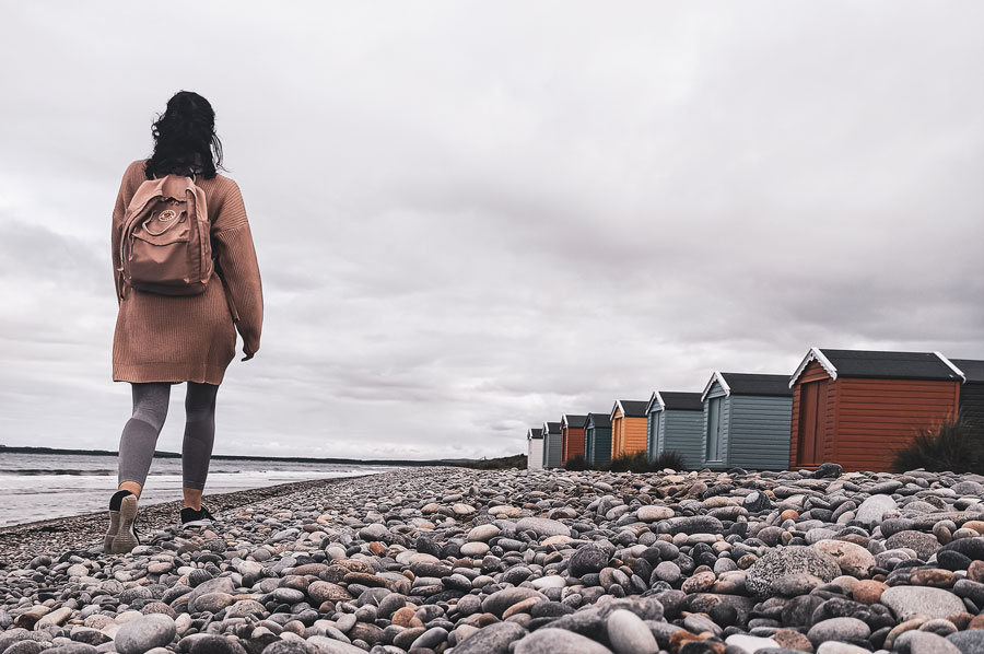 a girl walking along findhorn beach with huts in the background