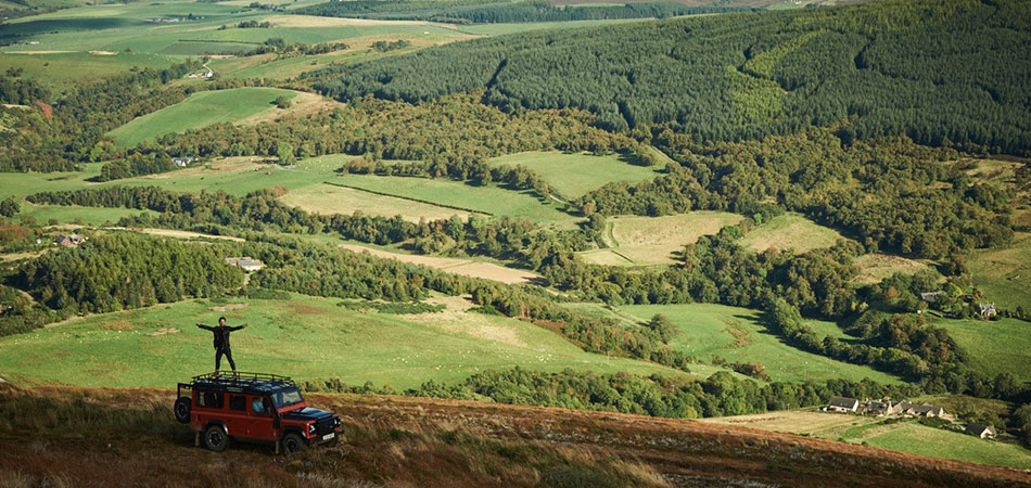 Man standing on top of car with forest backdrop