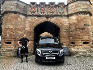 Man in Kilt stood next a car and a castle